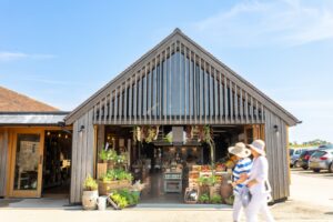 A shop with the bifolding doors wide open showing fresh and jarred produce on tabes and in baskets, and two people walking in front of the shop.