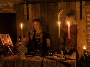 A DJ performing by candlelight with a second DJ dancing alongside her